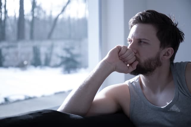 a sad man is thinking while sitting next to the window