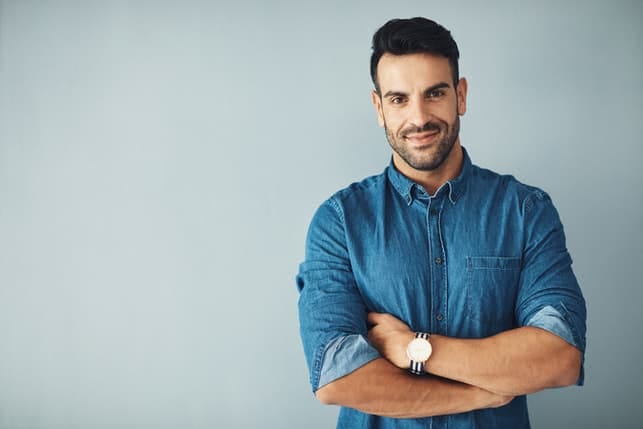 a confident man in a blue shirt is posing on a grey background