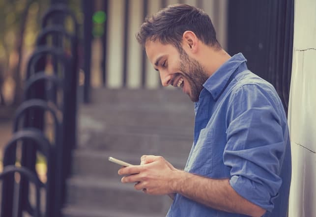 a handsome bearded man reading the messages from his girlfriend while smiling