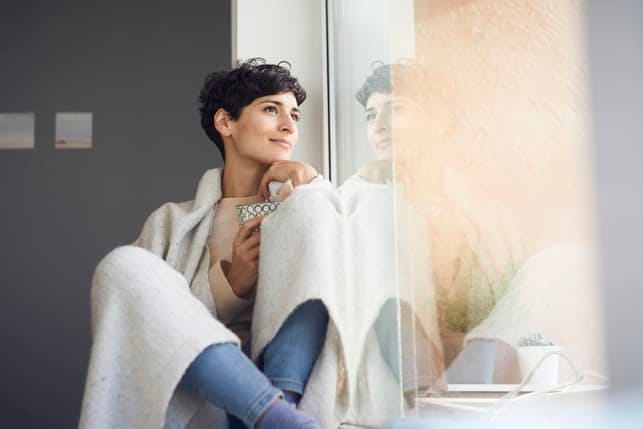 a woman is sitting on the windowsill and thinking while smiling