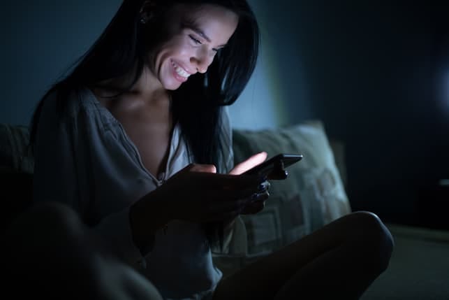 a happy woman is checking her smartphone while smiling