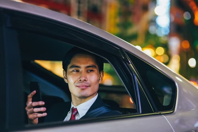 an attractive asian businessman checking his phone while sitting in his car